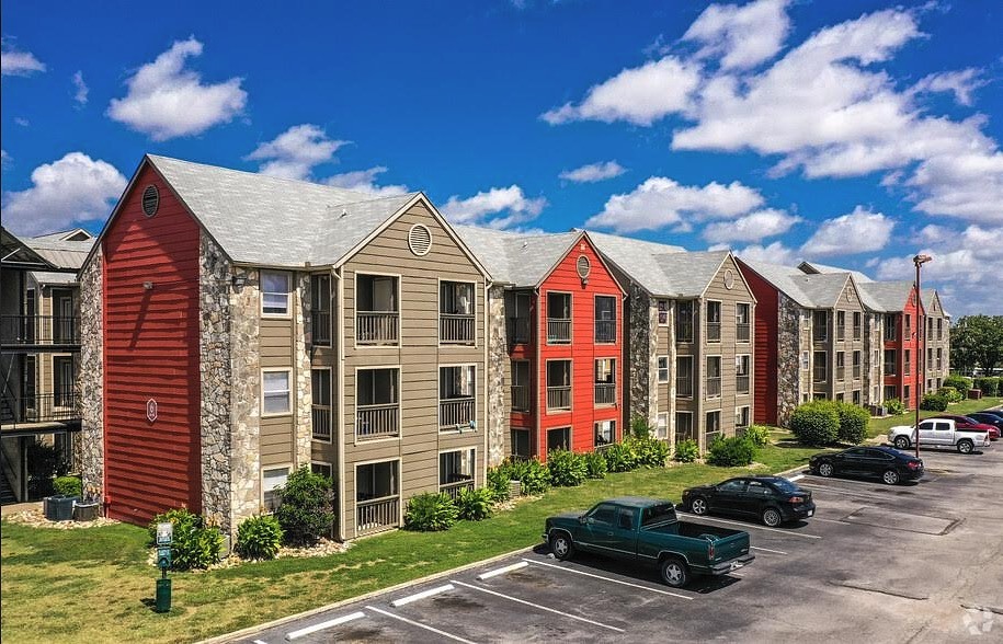 A row of red and beige buildings with cars parked in front.